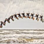 A sequence of images shows a kiteboarder performing a jump and trick over rough, choppy ocean waves, forming an arc in the sky. The cloudy sky and turbulent sea emphasize the dynamic and intense nature of the sport.