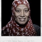 A Somali woman wearing a patterned hijab and dark clothing smiles softly at the camera against a dark background. The text reads, "Amira / Age: 60 / Somalia" and "I wish for my family to come here from Somalia so we can be reunited.