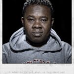 Portrait of a man wearing a grey hoodie with a neutral expression and looking directly at the camera. The text on the image reads: "Djiouong / Age: 33 / Ivory Coast" and below that: "I wish to forget what has happened and start a new, happy life.