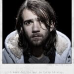 A young man with long hair and a beard looks directly at the camera with a serious expression. He wears a light-colored hooded jacket. Text below the image reads: "I wish for the war in Syria to stop." The name, age, and location, "Osman, Age: 23, Syria," are in the top right corner.