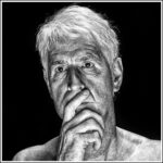 Black-and-white portrait of an older man with white hair, gazing pensively ahead. His right hand covers part of his mouth and chin. The background is dark, highlighting the details and expression on his face, suggesting deep contemplation.