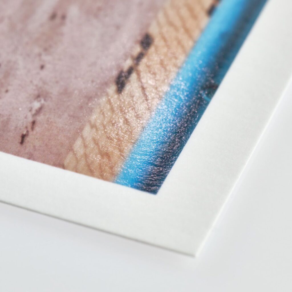 Close-up of a printed photograph on glossy print paper, showcasing a brown textured surface with a blue strip along one edge. The photo is set against a white background.